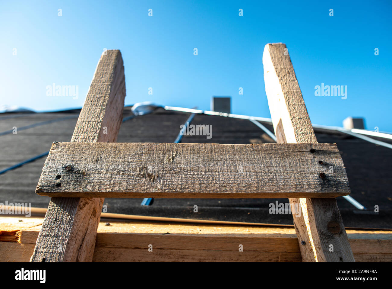 Wooden ladder on the roof of a house. Close-up wooden ladder. Sunlight. Concept of repair and construction of roof. Stock Photo