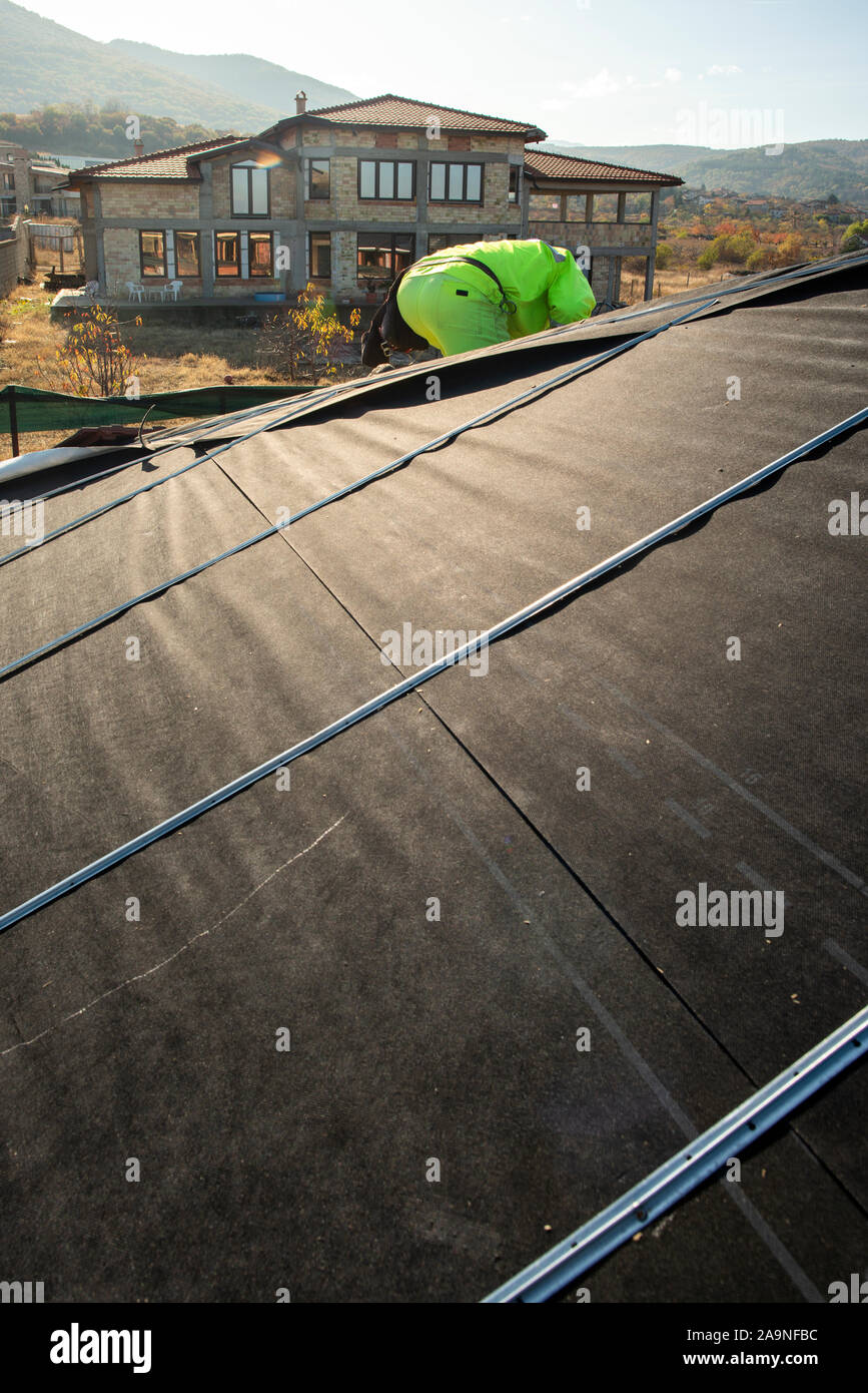 Worker on the top of the house making roof. Building a new house with black roof. Repair and build construction of roof. Conception for roofing, new h Stock Photo