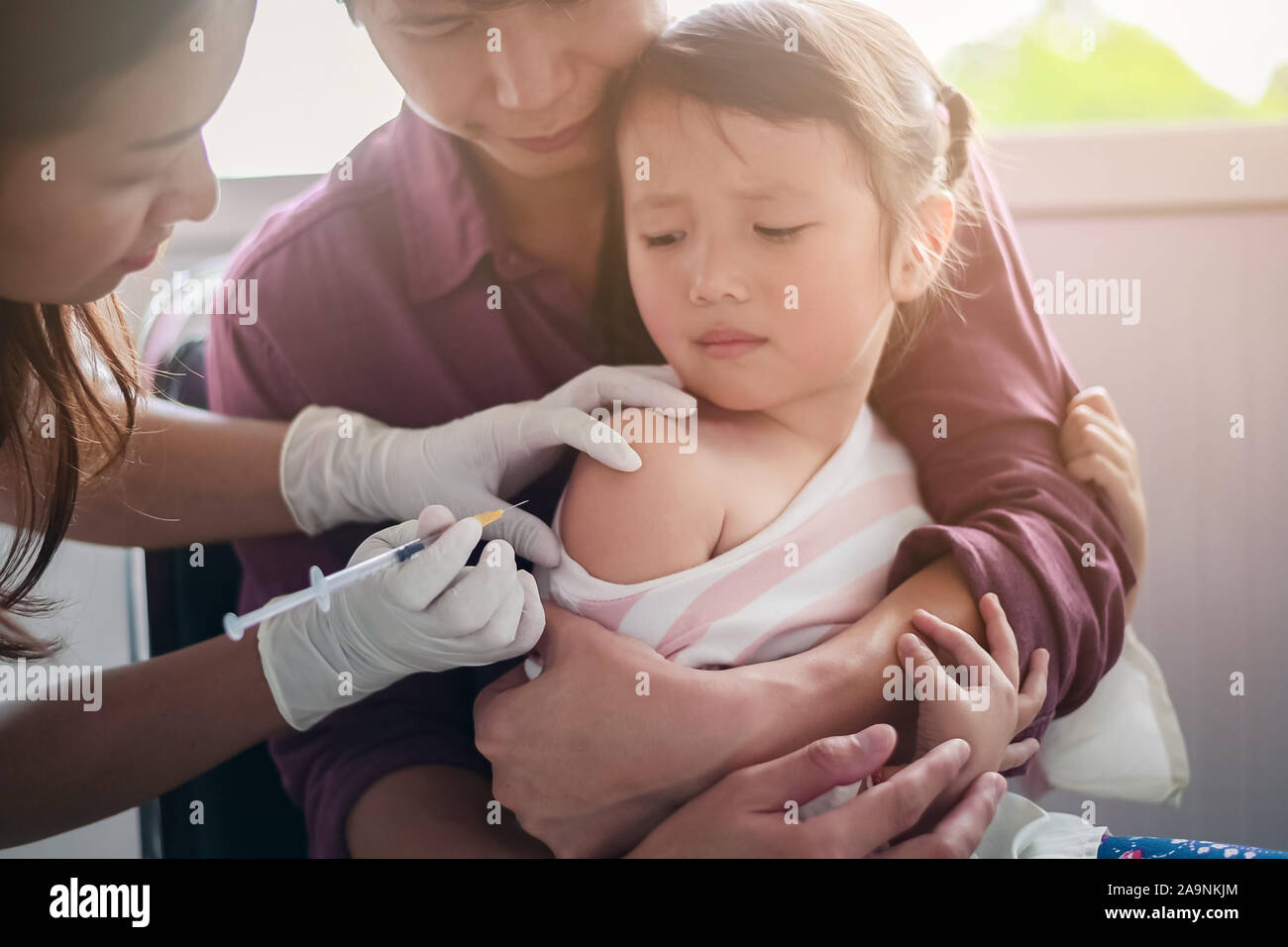 Little child having Injection,Close-up Doctor injecting vaccination to arm of asian little girl ,with the father hug the child, for not wriggle while Stock Photo