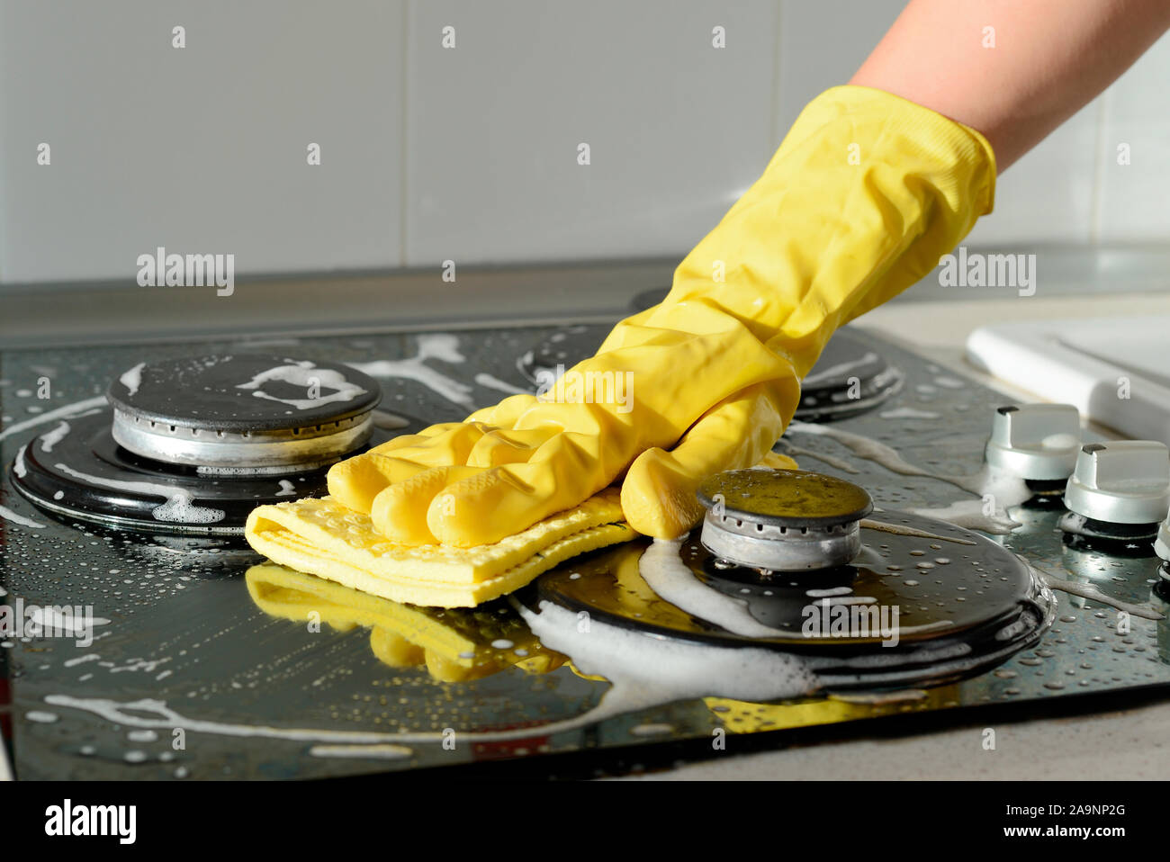 In A Yellow Rubber Glove A Hand Cleans A Gas Stove Kitchen