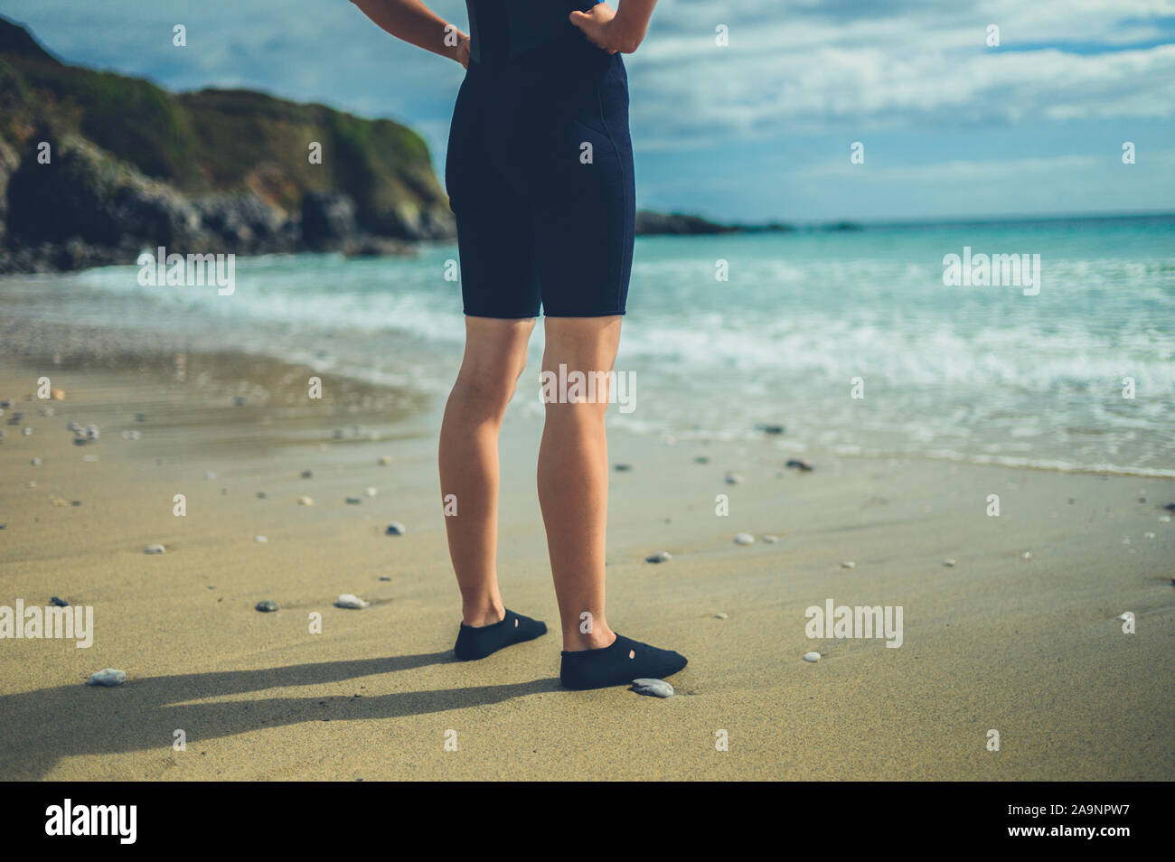 The legs and feet of a young woman wearing a wetsuit on the beach in