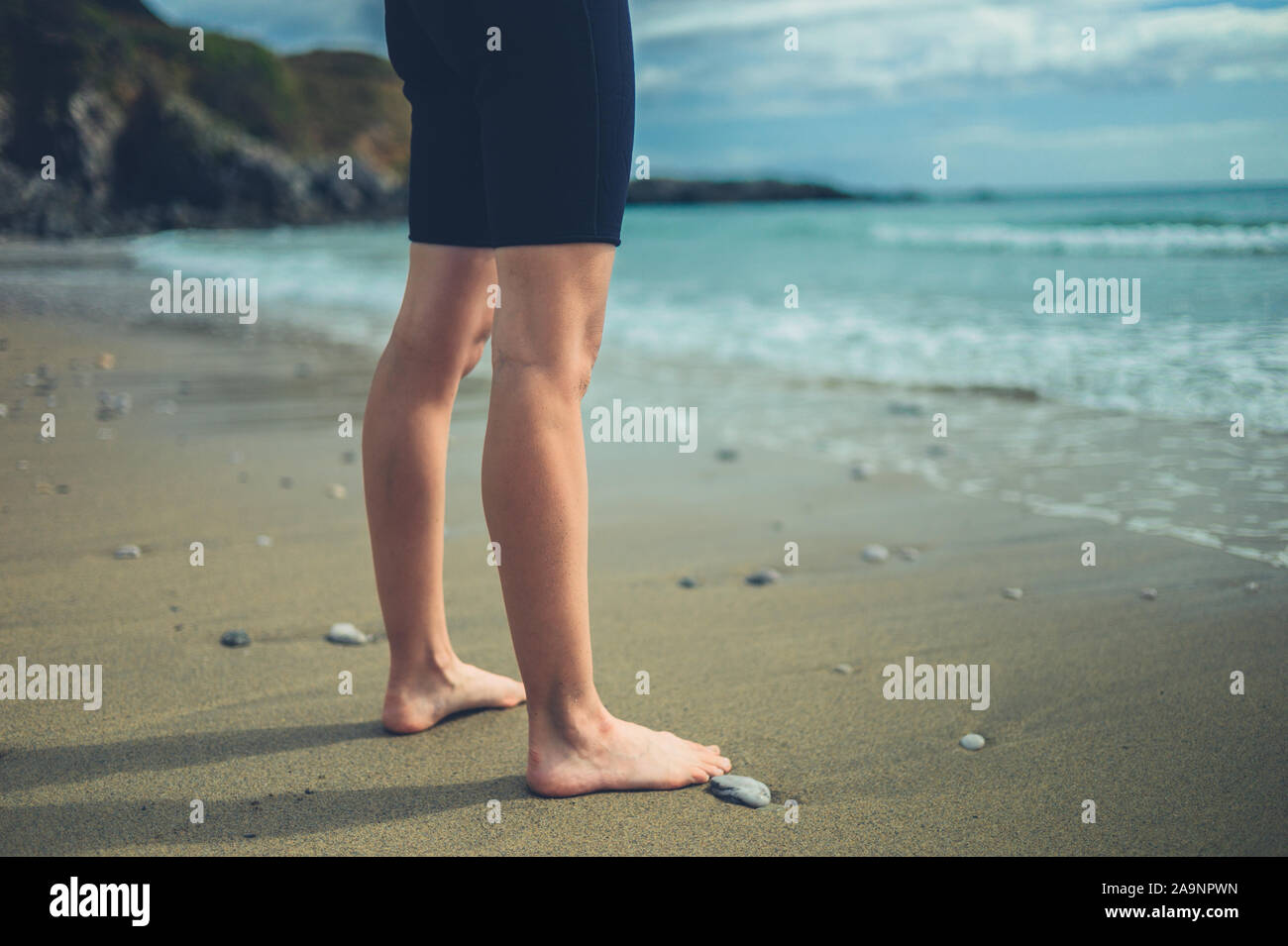 The legs and feet of a young woman wearing a wetsuit on the beach in