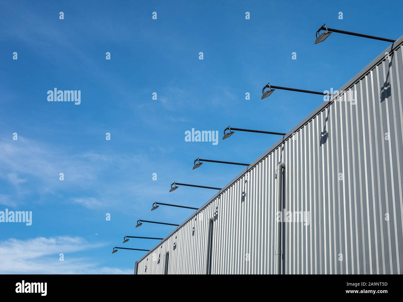 Street architecture outdoor lamp hanged and cantilevered from the wall of the building which is metal sheet with blue sky background. Stock Photo