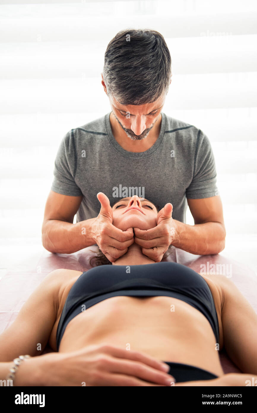 Osteopathic manipulation on digastric muscle demonstration. Male doctor examining muscles of woman patient with his fingers under her chin Stock Photo