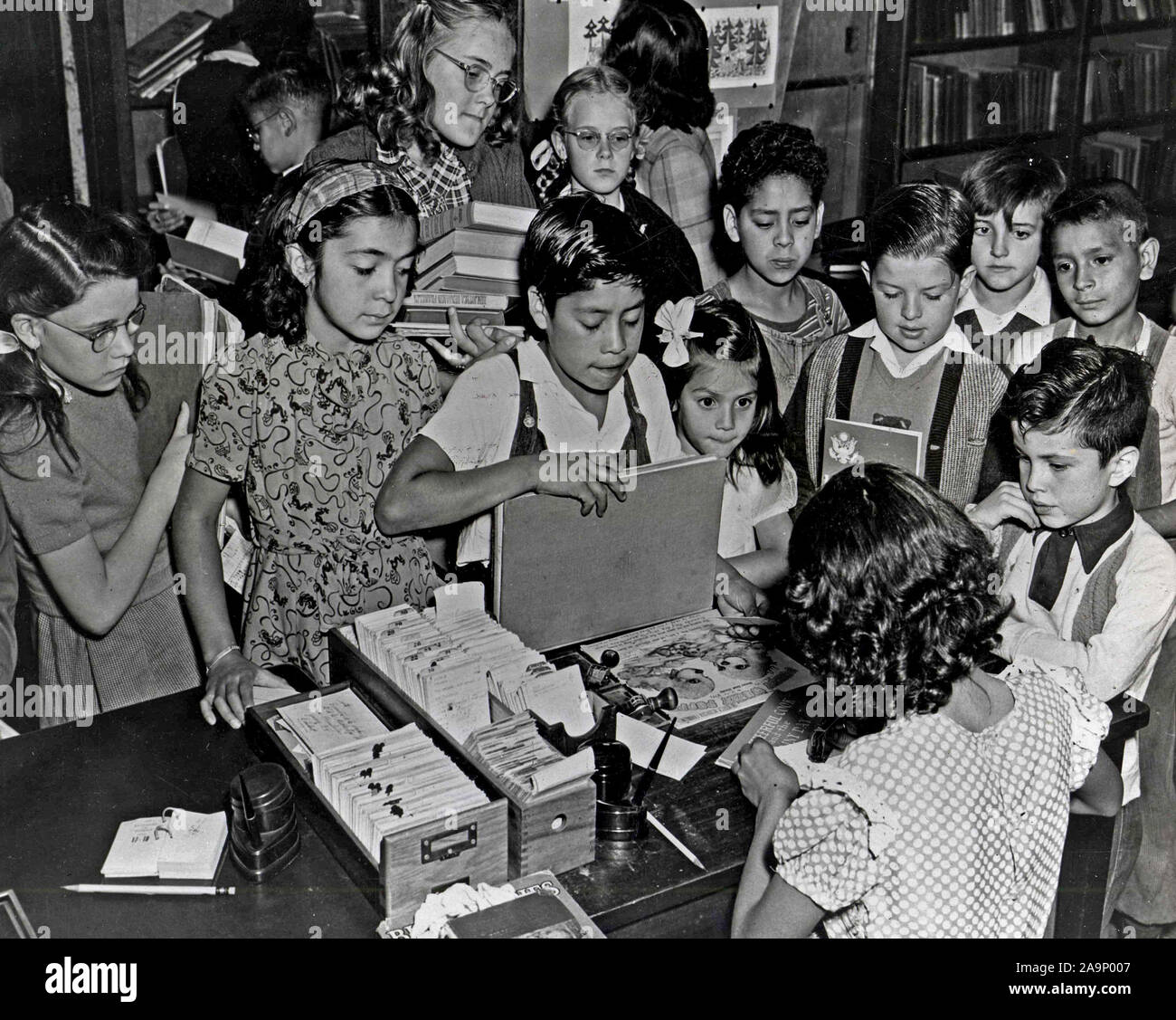 Children wait patiently to have their books signed out by circulation attendants.All previously attended the Saturday afternoon free movies at the Library's auditorium. Stock Photo