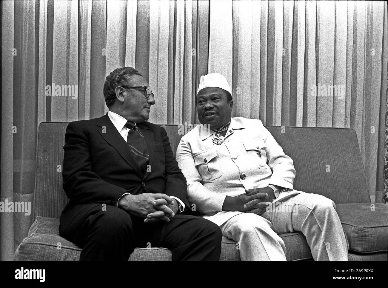 1976, April 30 – Executive Mansion – Monrovia, Liberia (Africa) – Henry Kissinger, William T. Tolbert Jr. – seated together on sofa, talking, laughing – Secretary of State Trip to Africa; Stock Photo