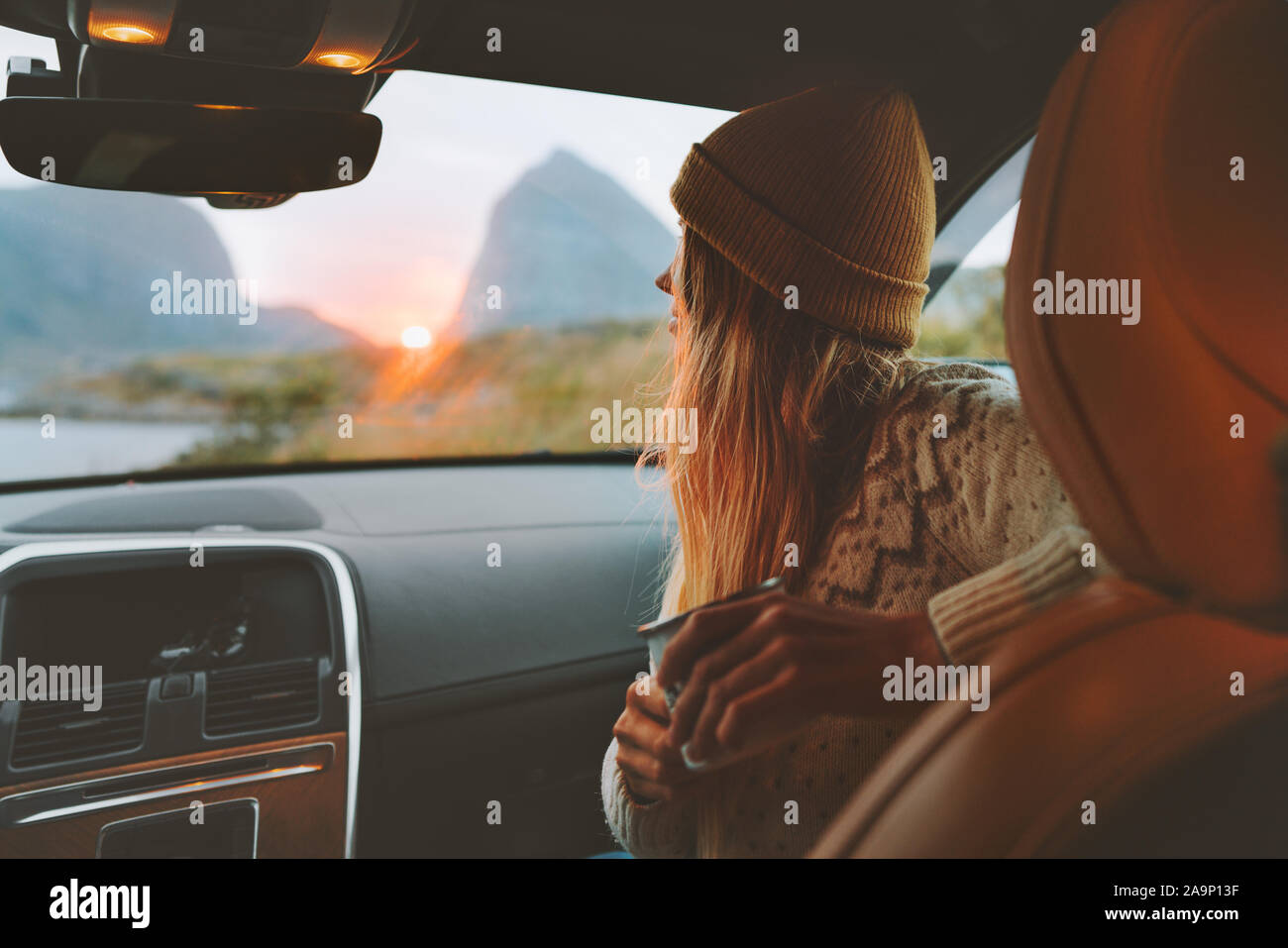 Woman on road trip traveling by rental car relaxing with coffee cup adventure lifestyle vacations vibes outdoor sunset Norway mountains view in window Stock Photo
