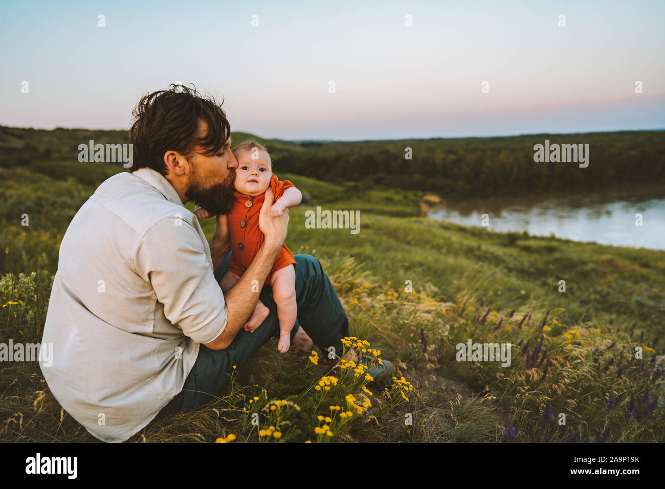 Father kissing baby daughter walking outdoors happy family lifestyle dad and child sitting on grass together summer vacations parenthood childhood con Stock Photo
