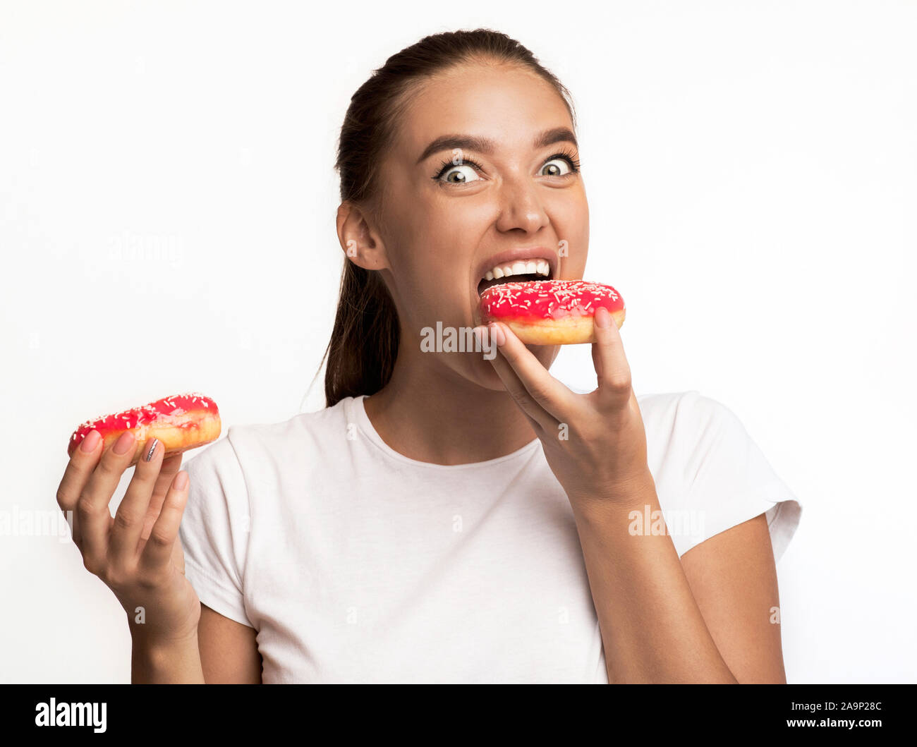Hungry Girl Eating Donuts Standing Over White Background Stock Photo
