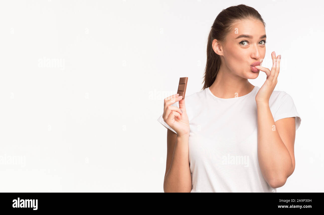 Girl Eating Chocolate And Licking Finger Standing On White Background Stock Photo