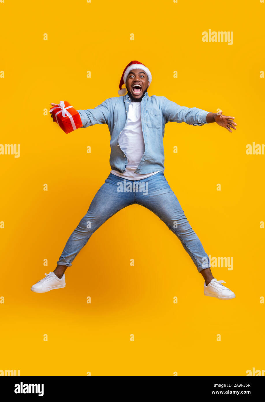 Overjoyed afro guy in santa hat jumping with gift box Stock Photo