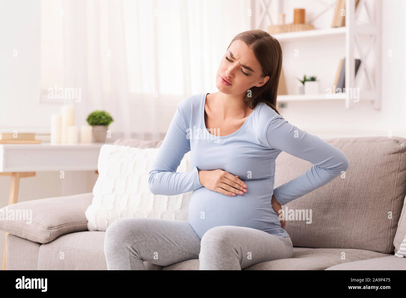 Pregnant Girl Suffering From Backache And Spasms Sitting On Couch Stock