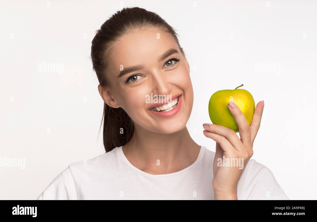 Smiling Girl Holding Apple Standing On White Background, Studio Shot Stock Photo