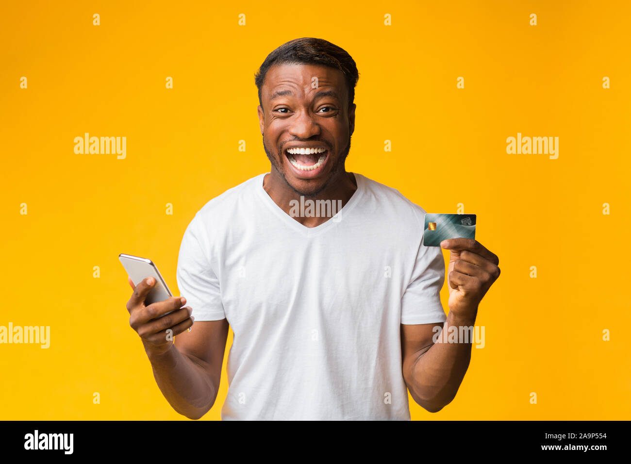 Happy Man Holding Smartphone And Credit Card Standing, Studio Shot Stock Photo