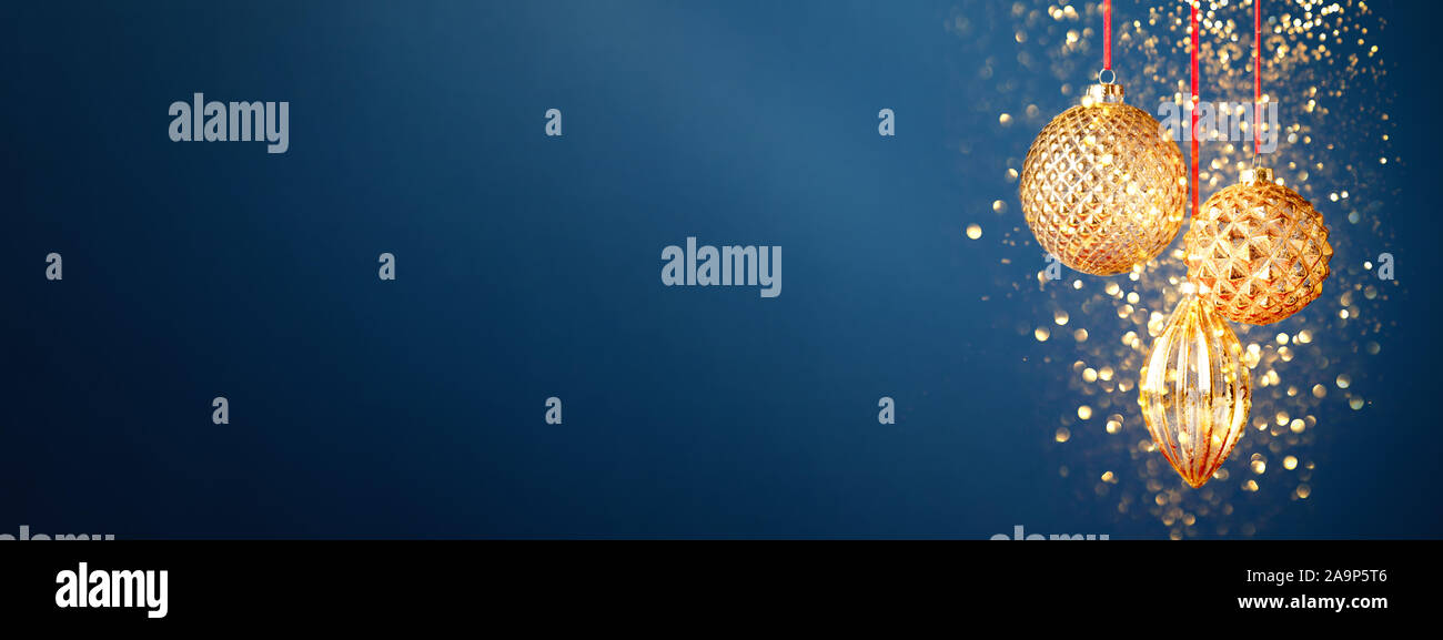 Three golden Christmas baubles hanging against the dark blue background ...