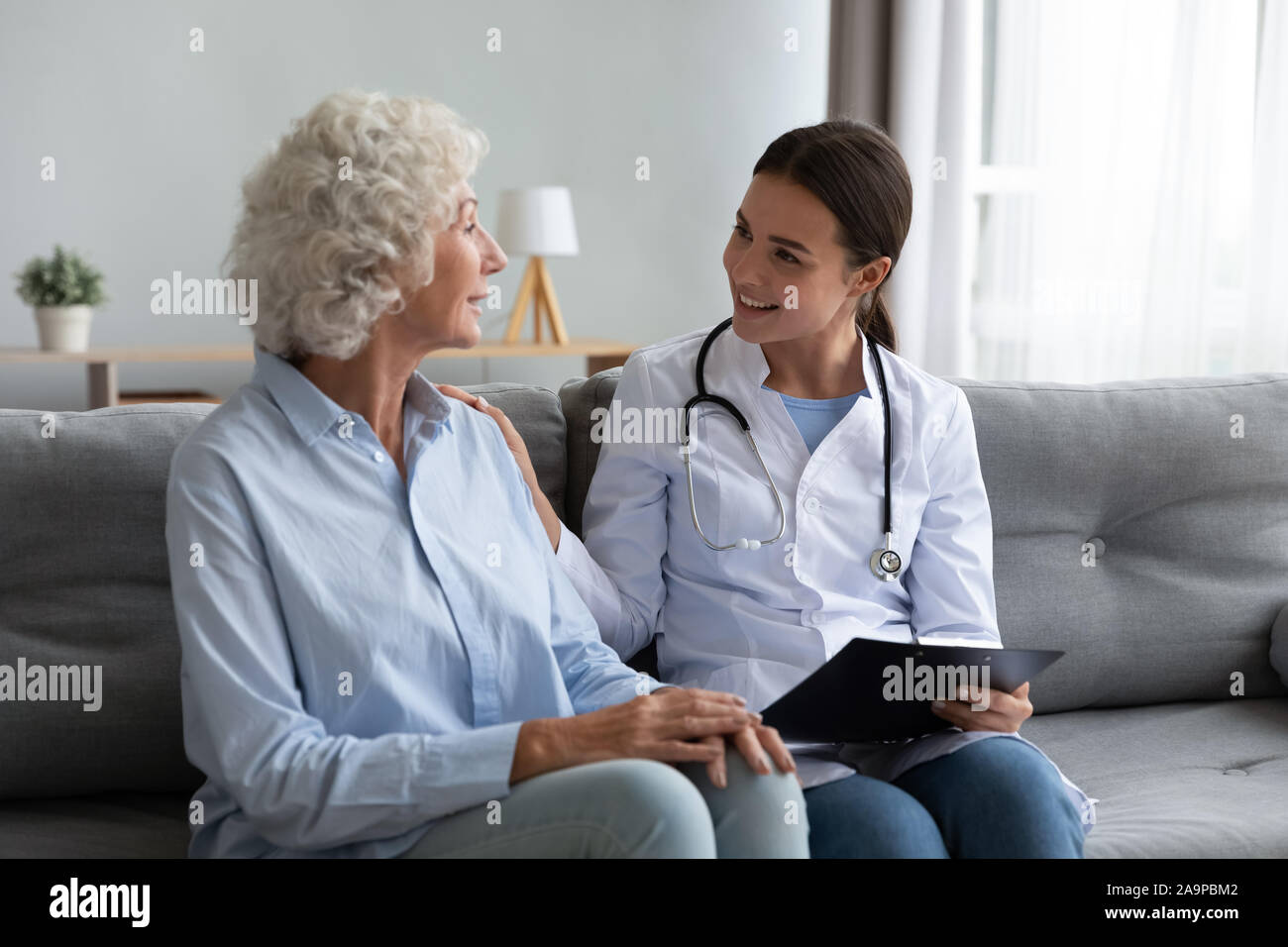 Caring young woman nurse helping supporting old adult grandmother patient Stock Photo