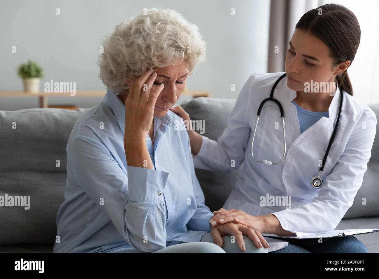 Young female nurse doctor comforting consoling sad old grandmother patient Stock Photo