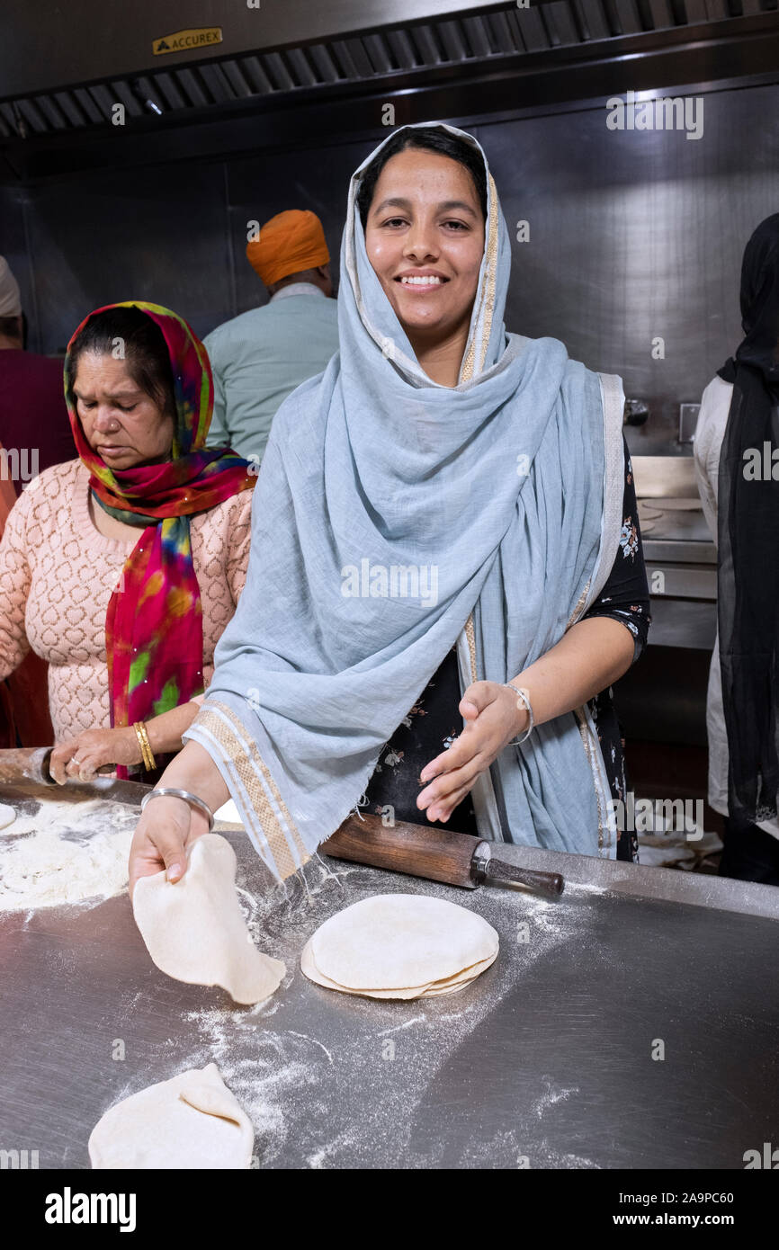 An attractive Sikh woman smiles while making roti breads in a Langar, a free communal kitchen. In South Richmond Stock Photo