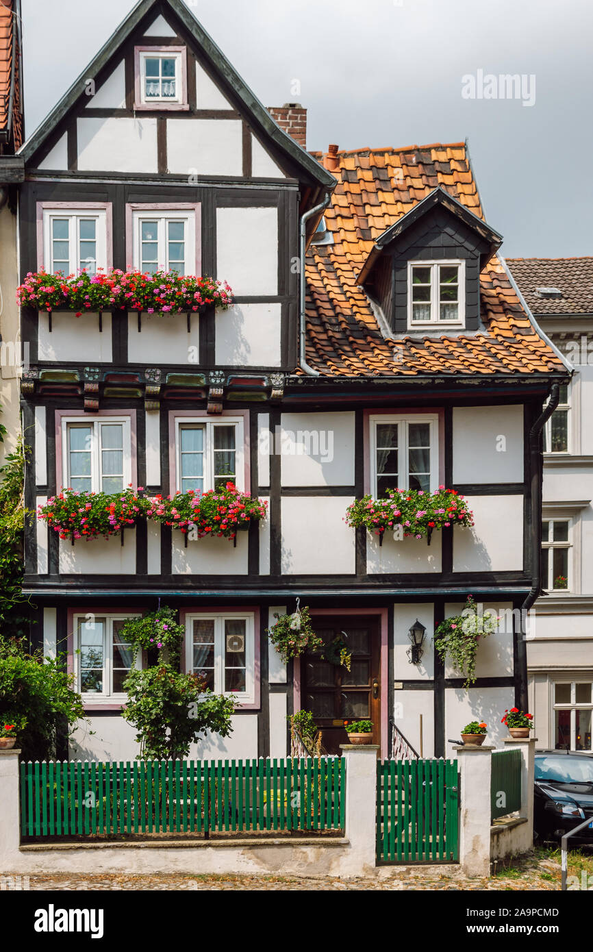 View of a traditional old German house with timber framing, windows decorated with red flowers and a green wooden fence in front of it, Quedlinburg. Stock Photo