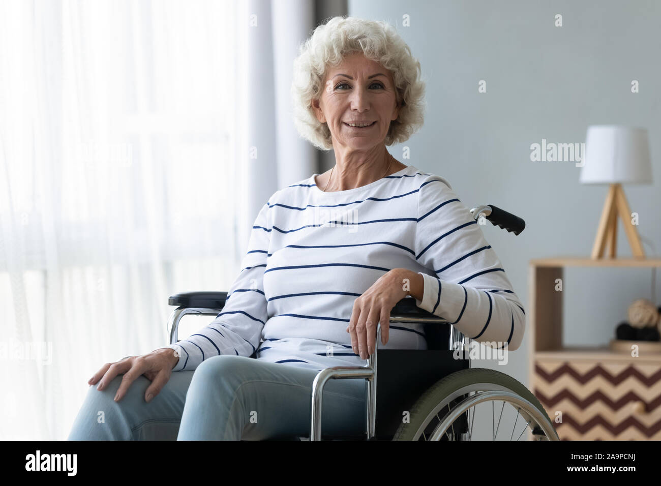 Happy disabled senior grandma sit on wheelchair looking at camera Stock