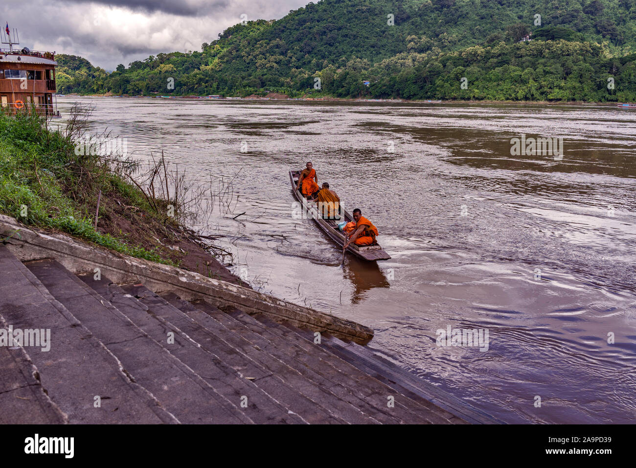 Three Monks in a boat resplendent in their saffron robes on the mighty Mekong River in the World Heritage Listed town of Luang Prabang in Laos Stock Photo