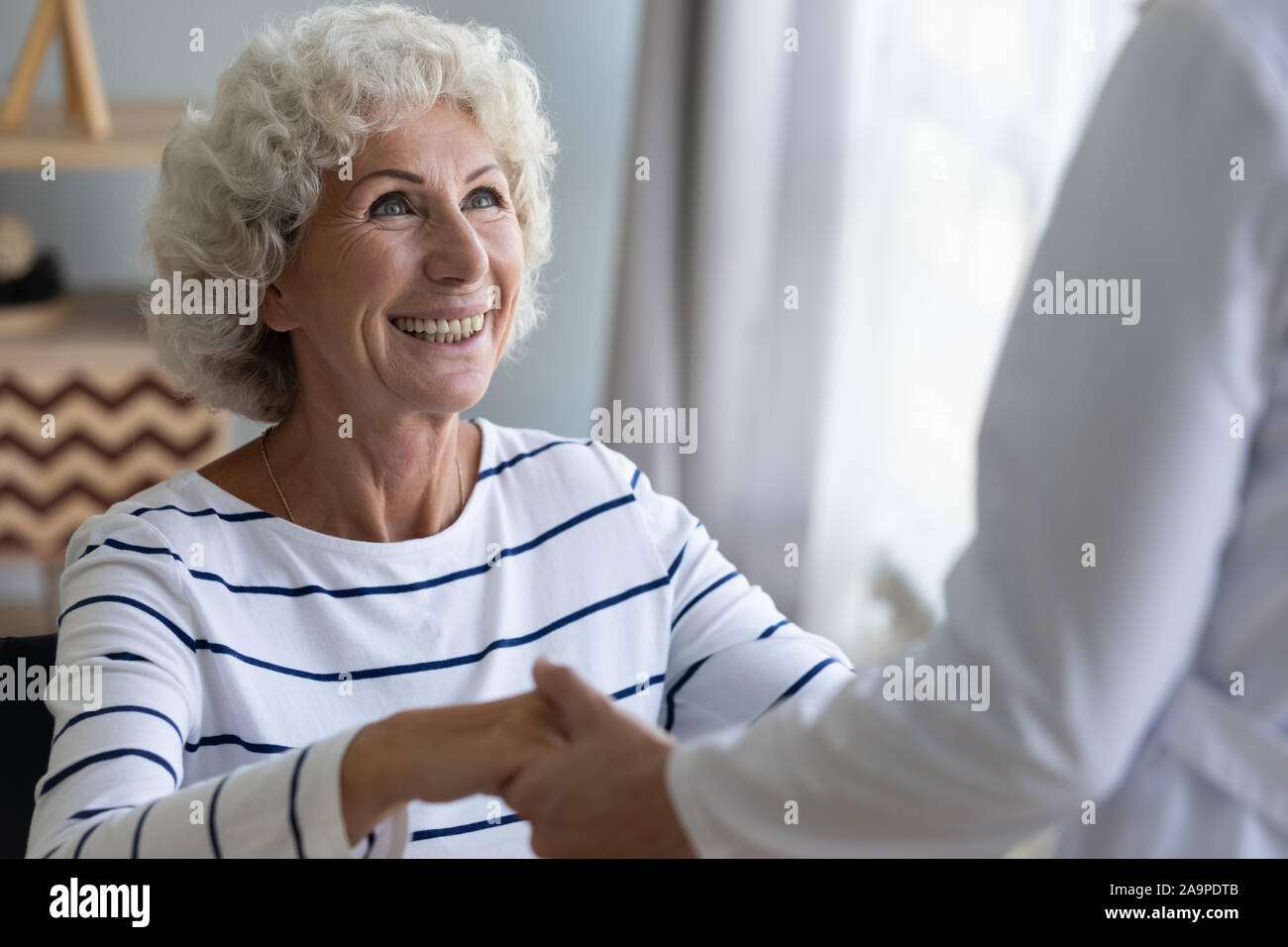 Happy grandma patient holding helping hand of caregiver getting up Stock Photo