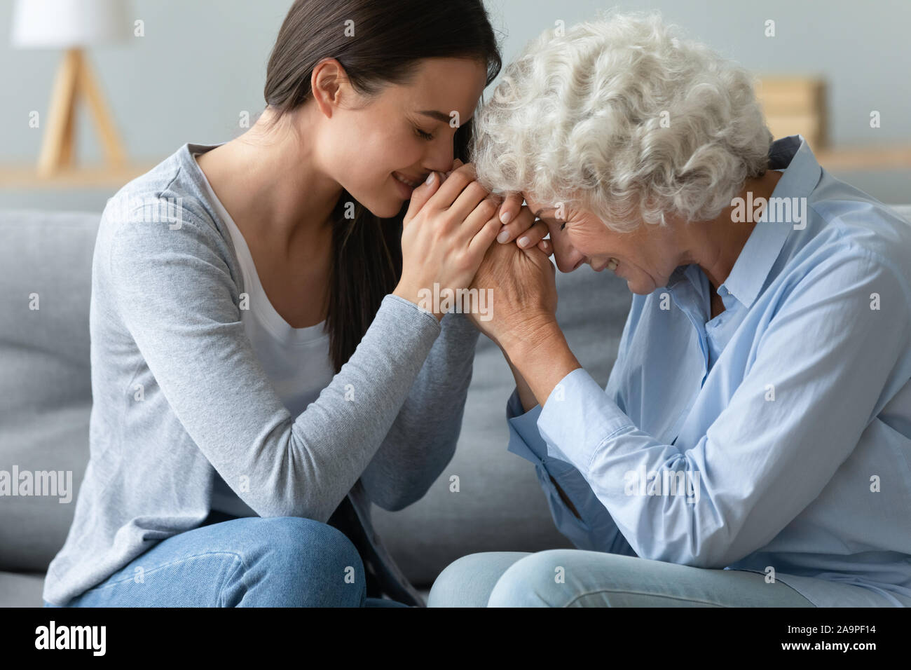 Caring young adult woman granddaughter hold hands of old grandmother Stock Photo