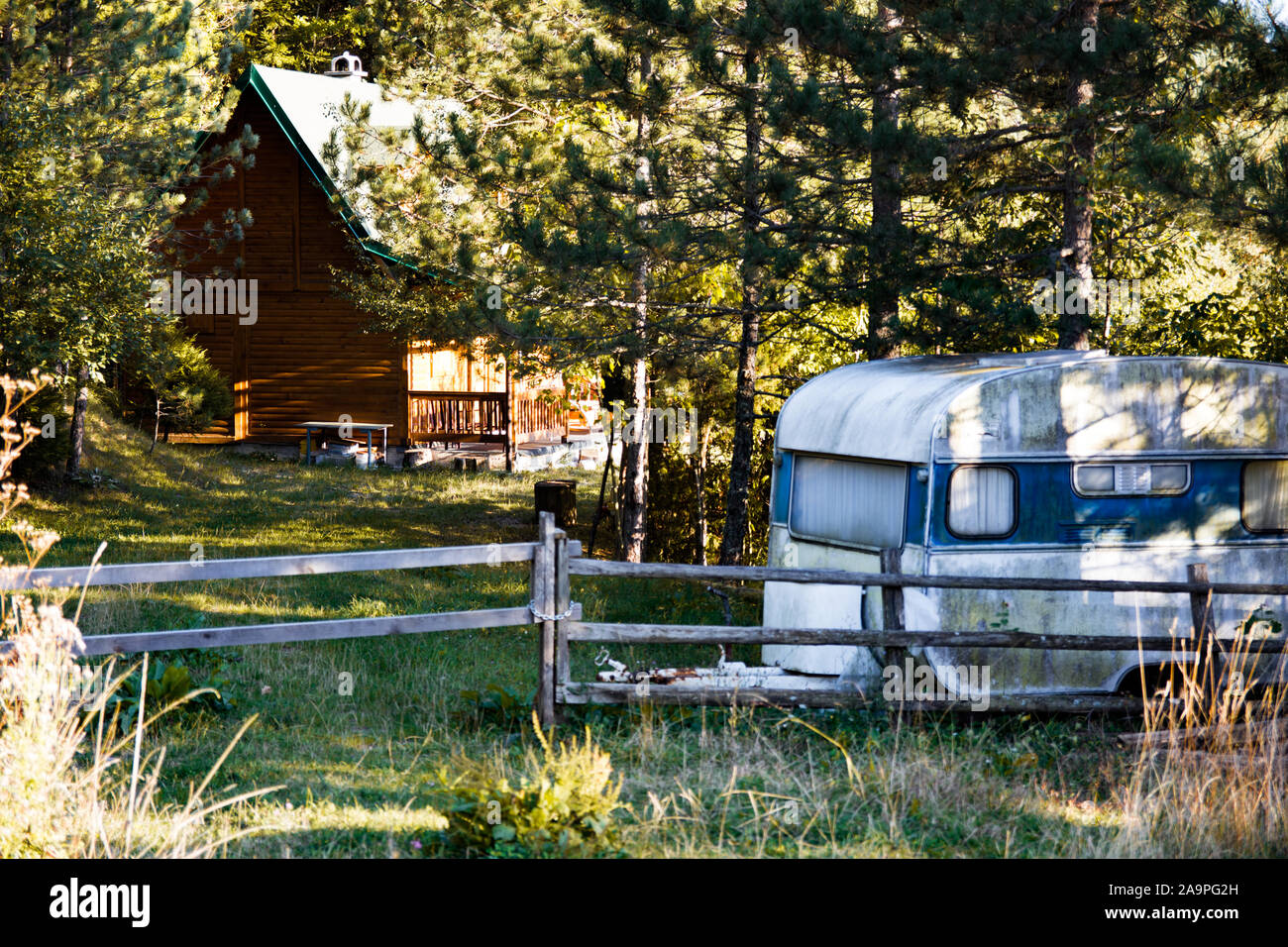 A Trailer And A Wooden House Or Log Cabin Covered By Sunlit Rays