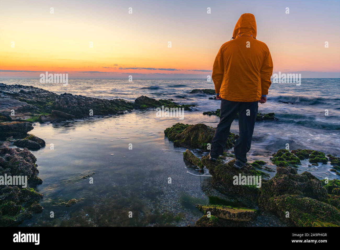 Azerbaijan, Baku - November 8, 2019: A young guy in a hood meets sunrise on the coast of the sea Stock Photo