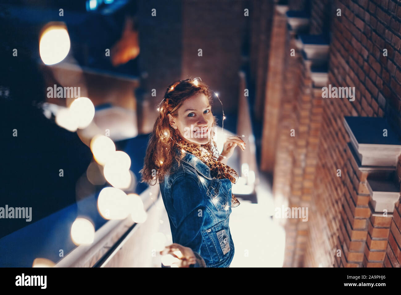 Happy young woman playing with fairy lights outdoors in city Stock Photo