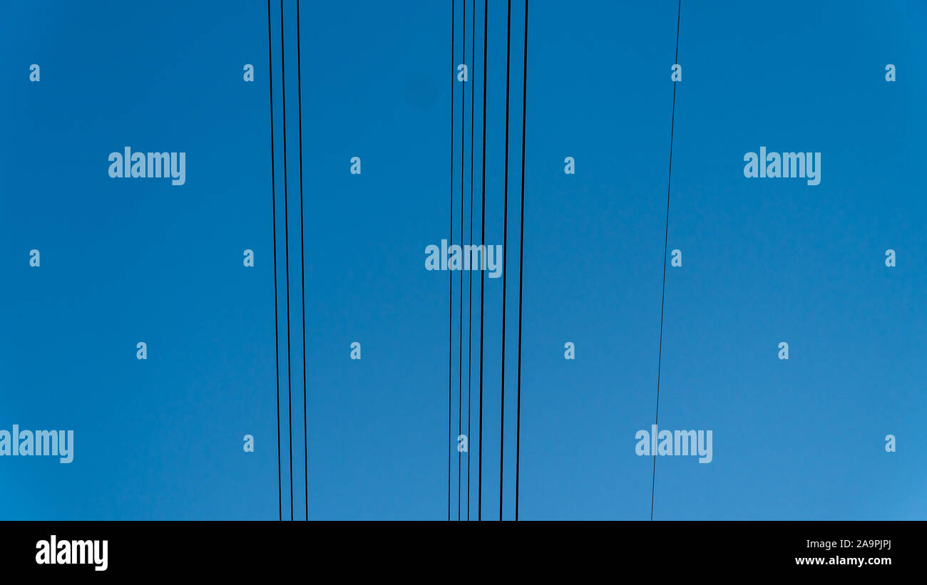 Overhead power lines. Electricity supply of the city. Cables against the blue sky. Parallel lines. Stock Photo