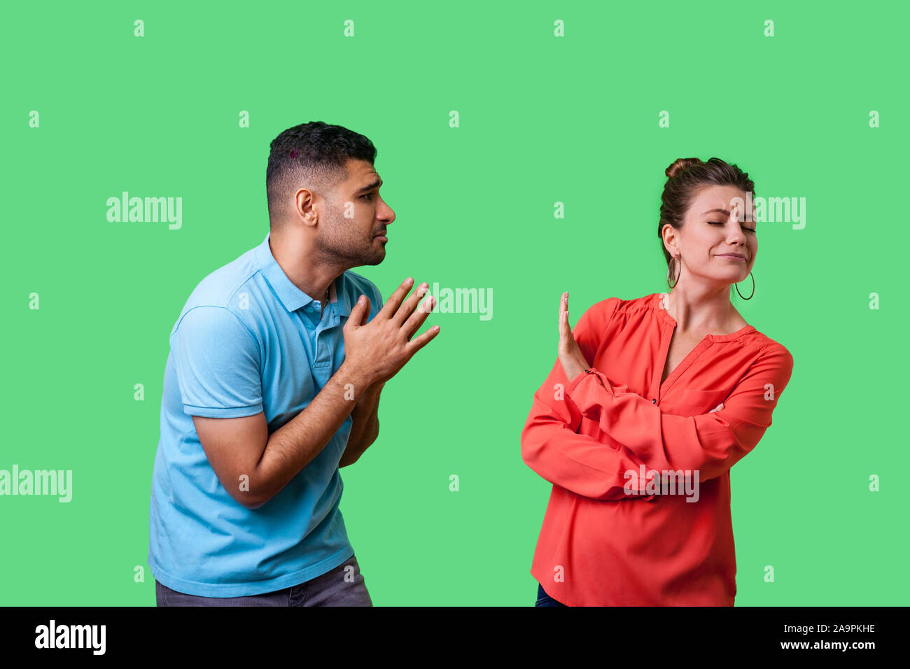 Portrait of funny couple in casual wear standing together, man holding arms in prayer and pleading forgiveness, looking with hope at naughty woman, is Stock Photo