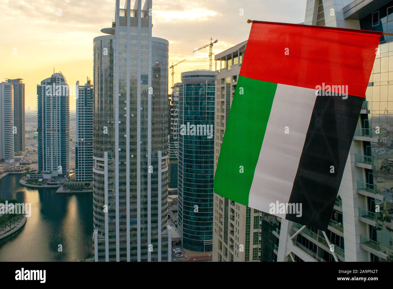Dubai / UAE - November 16, 2019: UAE flag waves on foreground of Dubai city. Aerial view. National UAE flag. Flag day Stock Photo