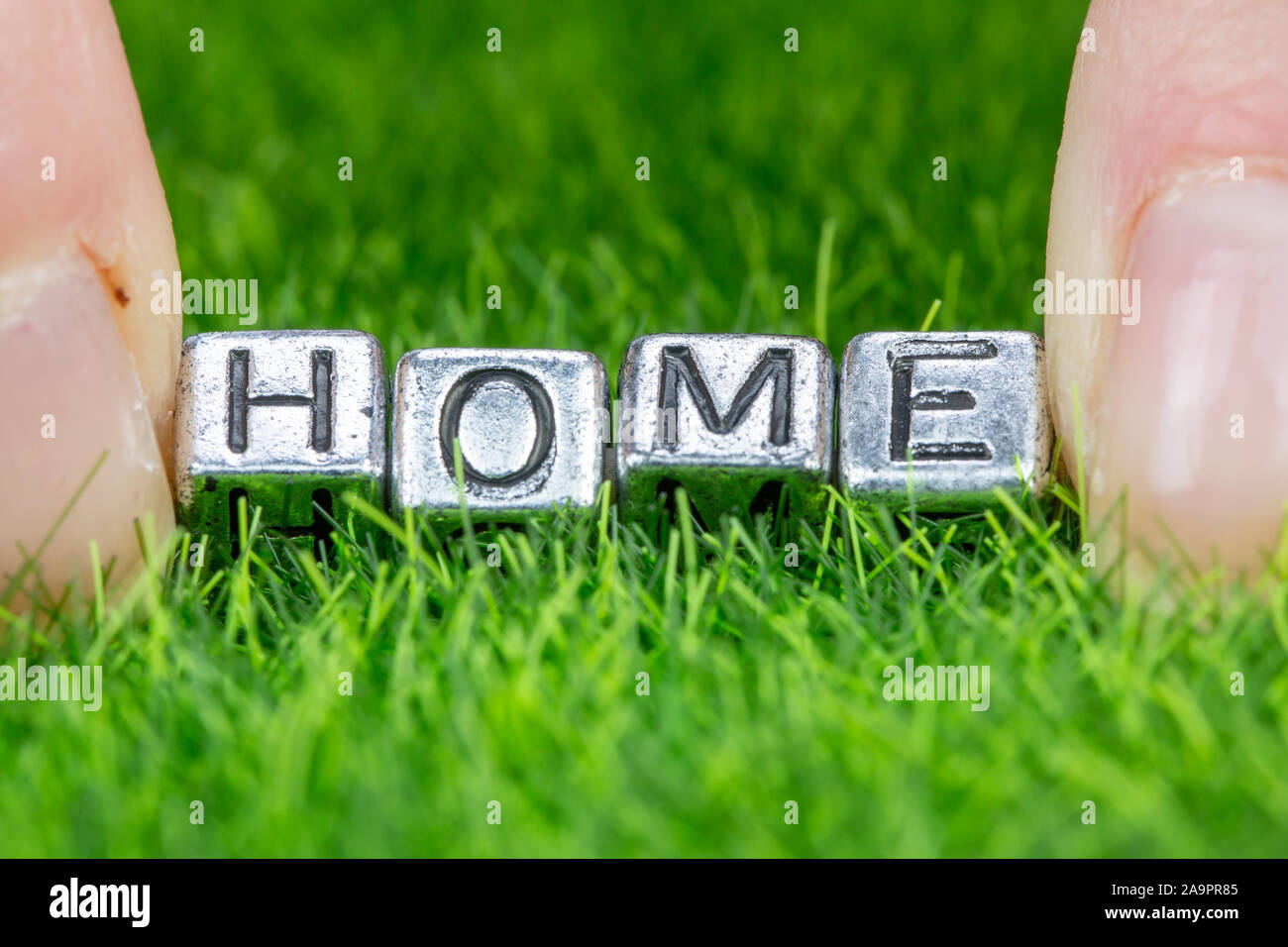Close up on word HOME written in metal letters laid on grass and held between the fingers of a woman. Concept of ecological house, house in the countr Stock Photo