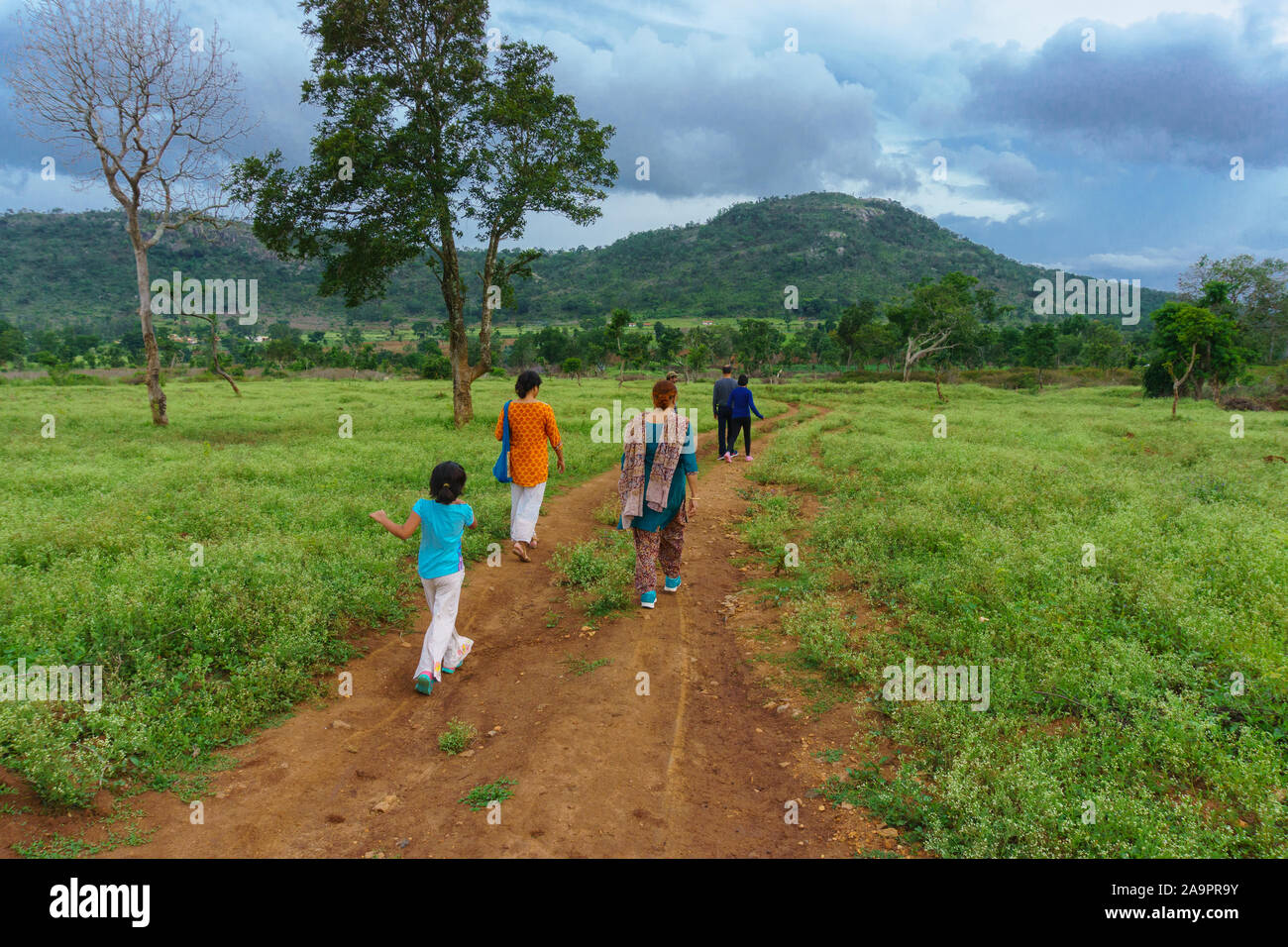 A Group of Travellers walking along a trail traversing through a meadow - photographed at the outskirt of Bandipur National Park (Karnataka, India) Stock Photo