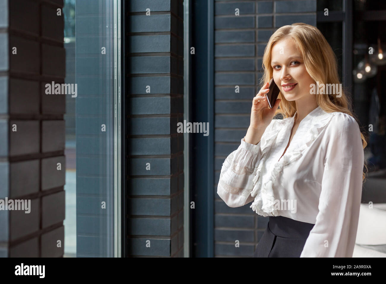 Portrait of happy successful businesswoman with long blond hair in stylish classic shirt smiling at camera and talking on cellphone, busy lifestyle. s Stock Photo