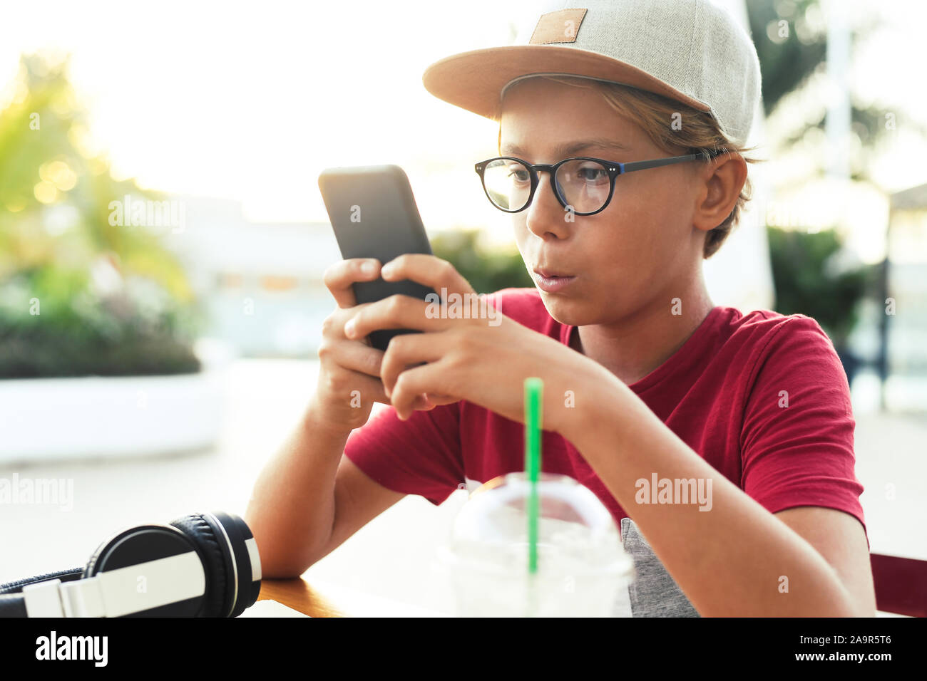 Teenager watching video on smartphone sitting at the table. Young boy  drinks smoothie outside at the bar using cell phone. Teen using mobile phone  rea Stock Photo - Alamy