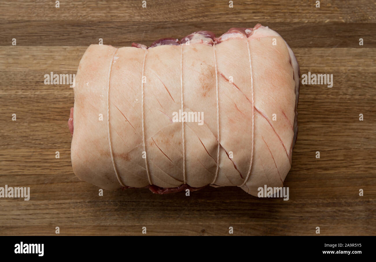 A close up of a raw cut of meat called a Pork Shoulder tied up and rolled with butcher's string with its skin scored ready for crackling on a wooden b Stock Photo