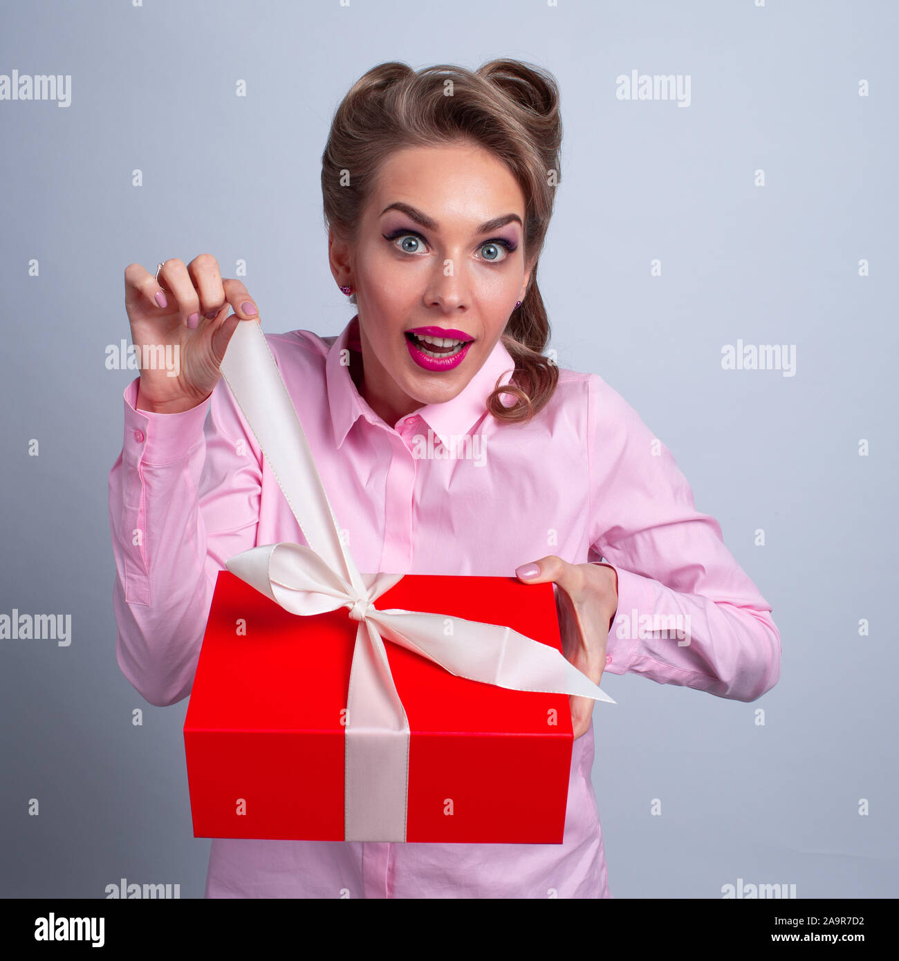 Hmm what is it! Funny woman pulling ribbon of bow on gift box and want to open. Christmas, new year, birthday, Valentine, Valentines day Stock Photo