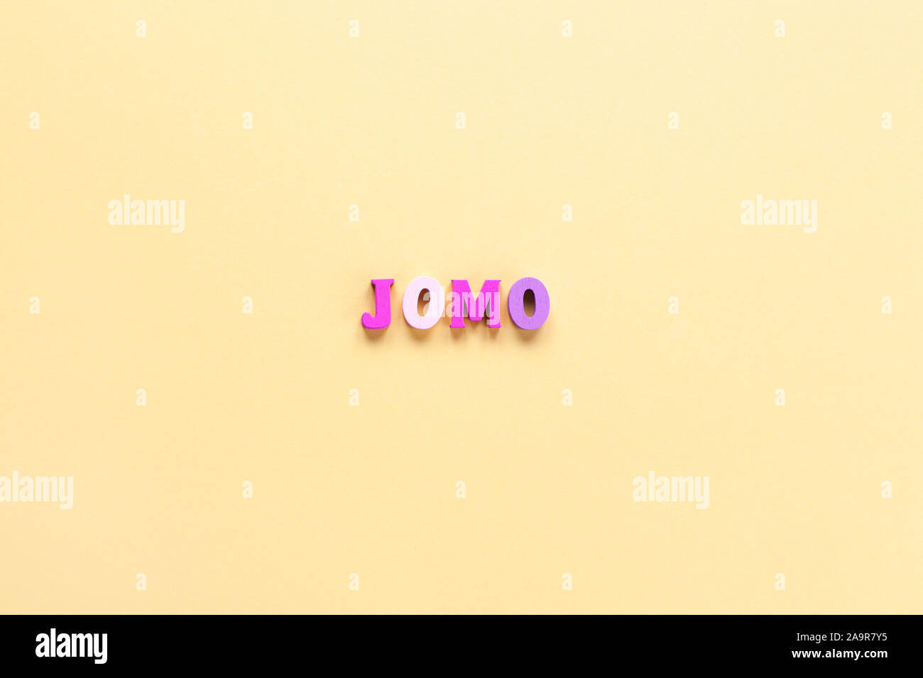 Abbreviation word JOMO in multicolored wooden letters on pastel yellow background. JOMO - Joy Of Missing Out. Opposition, choice, social problem, digi Stock Photo