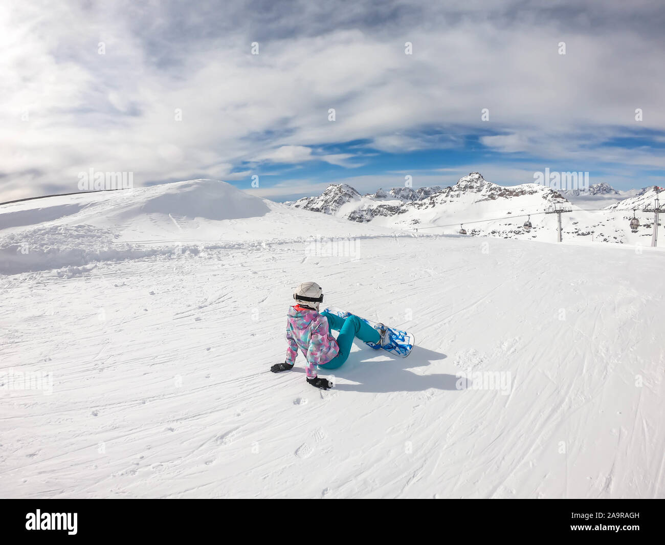 A snowboarder sitting on the slope in Mölltaler Gletscher, Austria. Perfectly groomed slopes. High mountains surrounding the girl wearing colourful sn Stock Photo