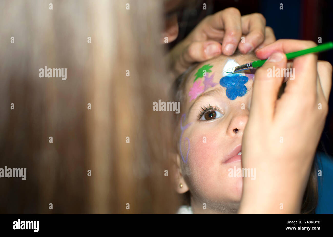 Face painting to a little girl at a birthday party. Mother paints her child's face with paint. Stock Photo