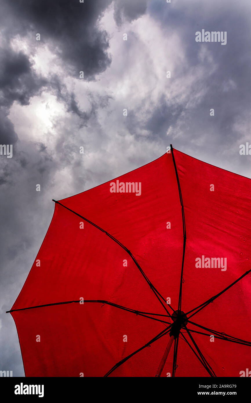 Looking up at a dark cloudy sky through a red umbrella Stock Photo