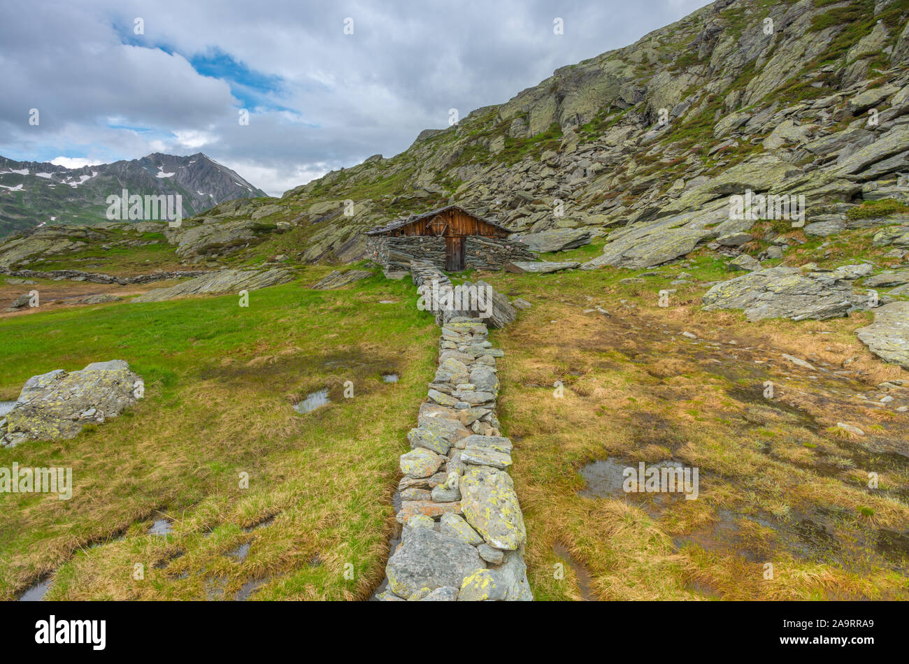 Old stone cabin along stone wall. Old mountain hut built of stone, sheepherder shelter up the mountains. Ancient dwellings in the Alps. Stock Photo