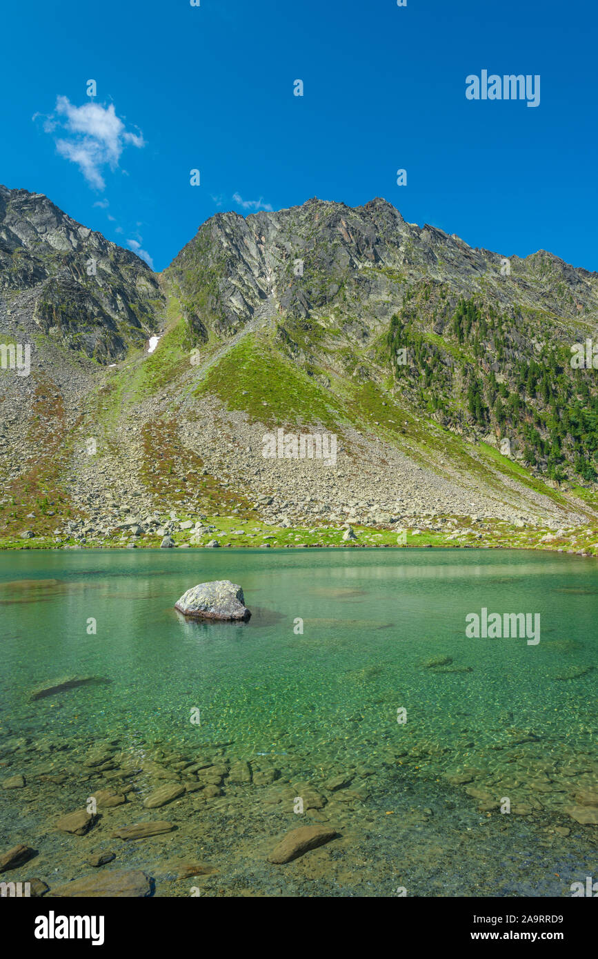 Wonderful emerald lake at Klausee, rugged mountains with landslide chute. Big lone boulder emerging from the lake. Stock Photo