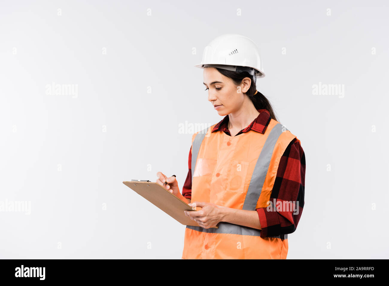Female builder in hardhat, flannel and working vest making notes in document Stock Photo
