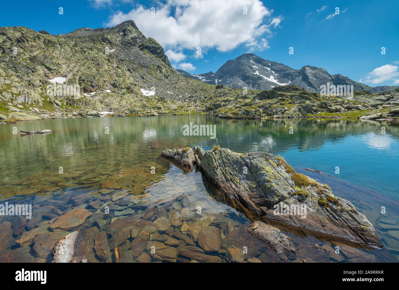 Pretty alpine tarn, beautiful mountain lake with mountains reflected in the calm water. Reflections of mountains and snow in mirror-still lake. Stock Photo