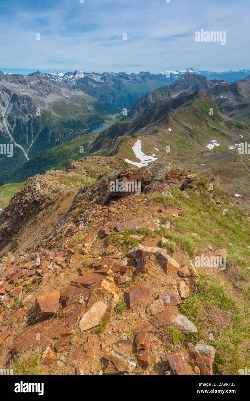 Views of the Italian - Austrian border at Passo Stalle from a redrock ridge. Red boulders with summer grass and a wall of snowcapped mountains. Stock Photo