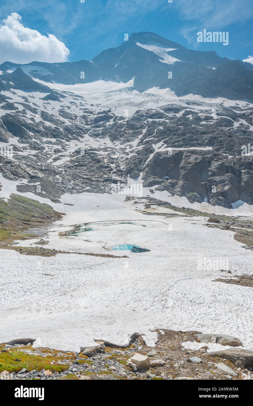 Turquoise lake created by melting ice and snow at the feet of an alpine glacier. Frozen, icy pond in the snow. Italian Alps during melting season. Stock Photo
