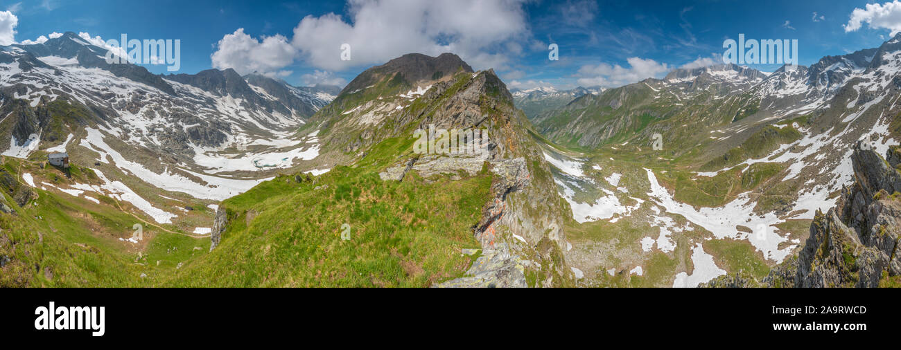 Commanding panoramic views of two valleys, panorama of a horseshoe valley in the Italian Alps. Summer day, snow patches in alpine, mountainous terrain. Stock Photo